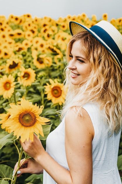 Garota loira feliz está sorrindo e segurando um girassol no campo de girassol.