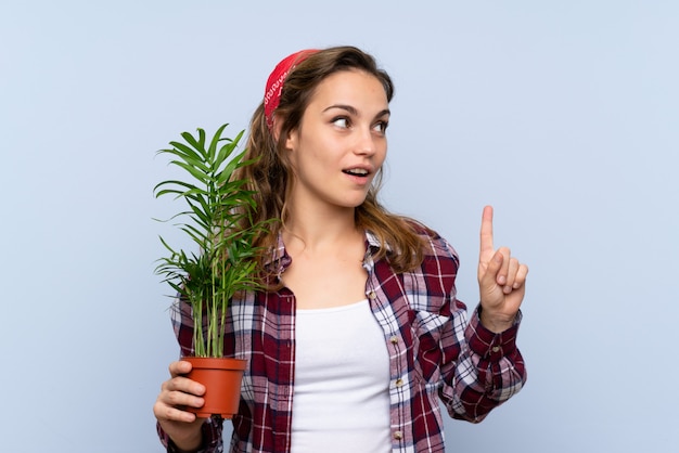 Garota loira jovem jardineiro segurando uma planta com a intenção de realizar a solução enquanto levanta um dedo