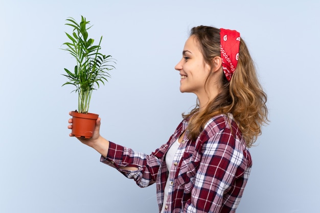 Garota loira jovem jardineiro segurando uma planta com expressão feliz