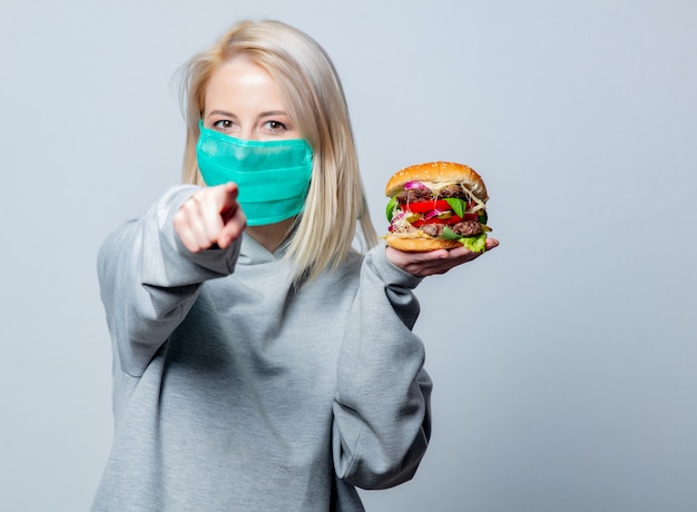 Garota loira na máscara facial com hambúrguer no espaço em branco