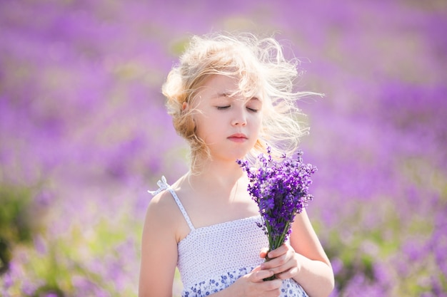 Garota loira no vestido cor no campo de lavanda com um pequeno bouqet nas mãos dela