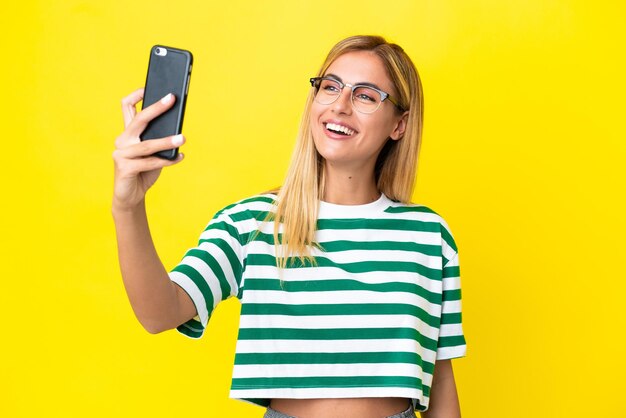 Garota loira uruguaia isolada em fundo amarelo fazendo uma selfie