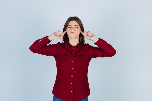 Garota mantendo os dedos atrás das orelhas em uma camisa casual e parecendo confusa