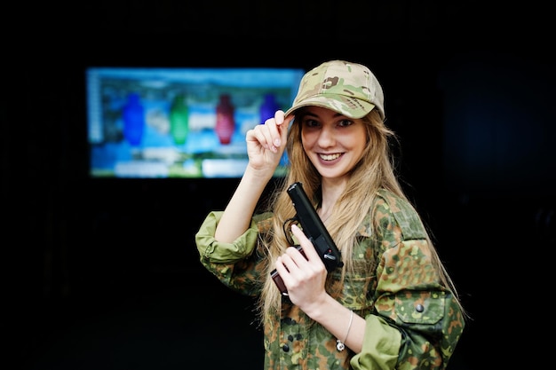 Garota militar em uniforme de camuflagem com arma na mão contra o fundo do exército no campo de tiro