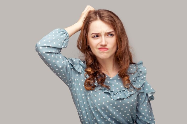 Foto garota morena confusa com blusa de babados coçando a cabeça tendo dúvidas, não tenho certeza contemplando