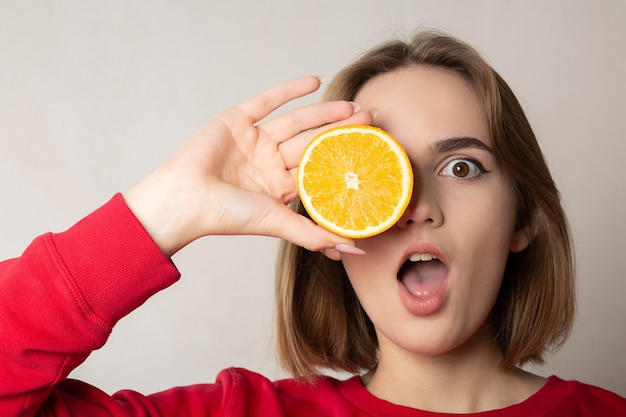 Garota morena legal posando com uma meia laranja, cobrindo um olho, contra uma parede branca. Espaço para texto