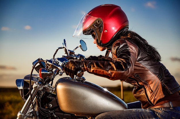 Garota motociclista em uma jaqueta de couro e capacete em uma motocicleta