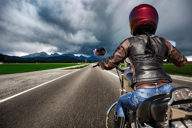 Foto garota motociclista em uma motocicleta descendo a estrada em uma tempestade de raios - forggensee e schwangau, alemanha baviera