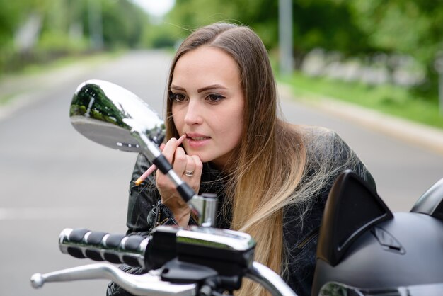 Garota motociclista pinta os lábios em uma motocicleta.