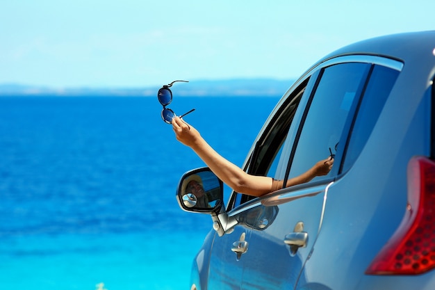 Garota motorista feliz com óculos de sol no carro no mar no verão