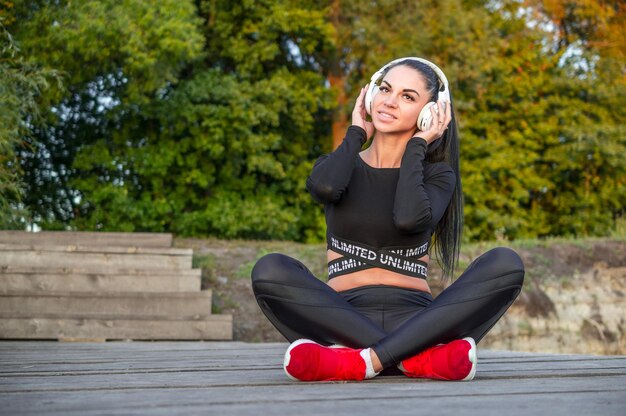 Garota muito desportiva com fones de ouvido ao ar livre./Muito jovem com fones de ouvido brancos.