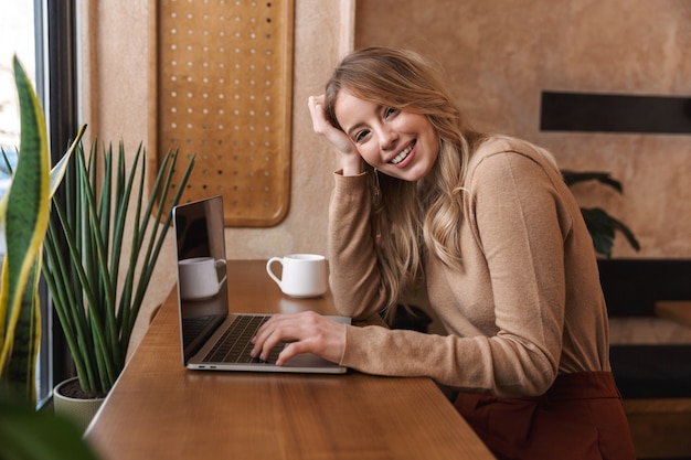 garota muito feliz sentada em um café usando um laptop