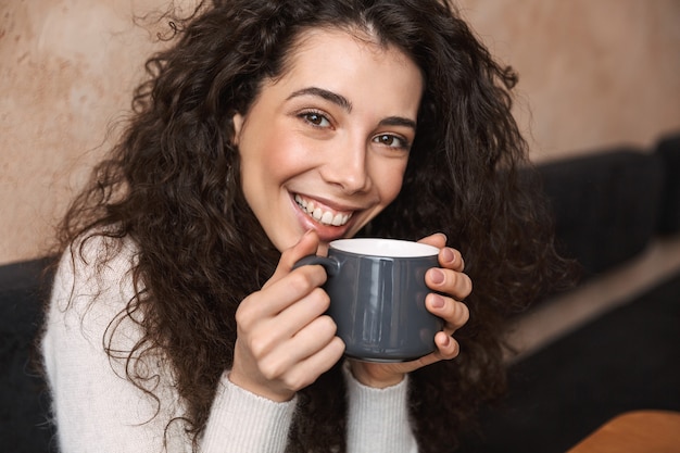 garota muito feliz sentada no café bebendo café segurando a xícara