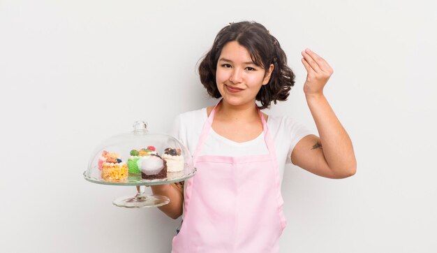 Garota muito hispânica fazendo gesto de capice ou dinheiro dizendo para você pagar o conceito de bolos caseiros
