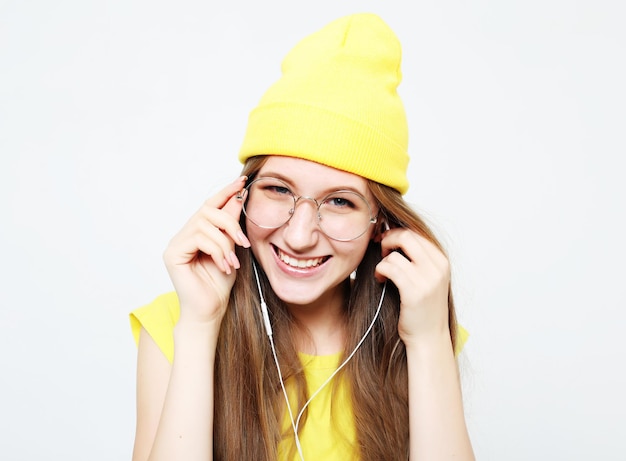 Garota muito legal de moda em fones de ouvido ouvindo música usando chapéu amarelo e camiseta