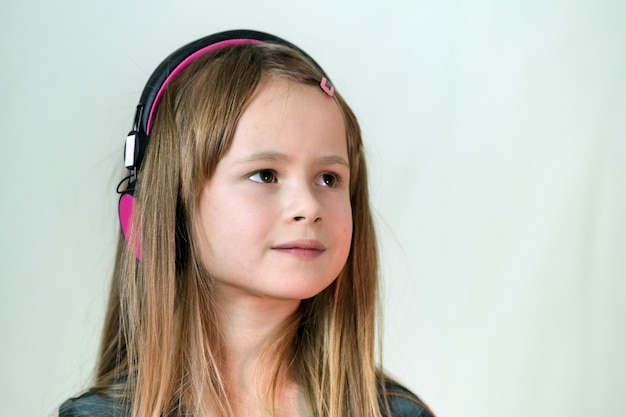 Garota muito sorridente cild ouvindo música em grandes fones de ouvido rosa.