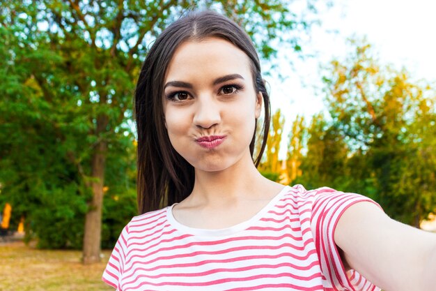 Garota muito sorridente fazendo selfie, morena de cabelos compridos em roupas brancas, closeup.