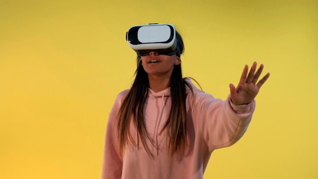 Garota multirracial usando óculos de realidade virtual em pé contra um fundo amarelo