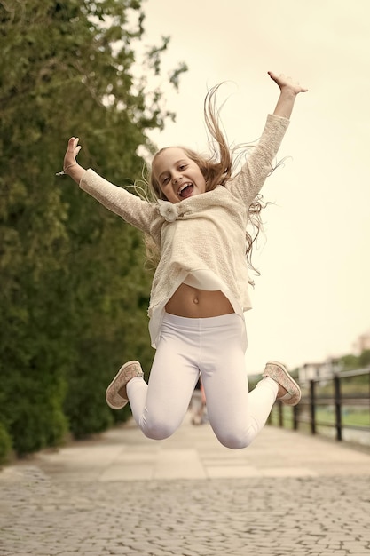 Garota na natureza de rosto sorridente feliz no fundo Conceito de felicidade Garota com expressão alegre salta no dia internacional da criança Criança feliz e alegre gosta de passear no parque