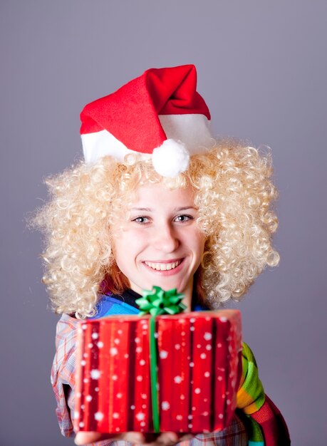 Garota na peruca loira e chapéu de Natal mostrar presente. Tiro do estúdio.