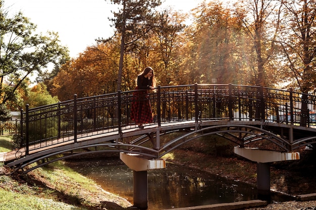 Garota na ponte com vestido vermelho longo escocês Garota com longos cabelos castanhos no parque outono