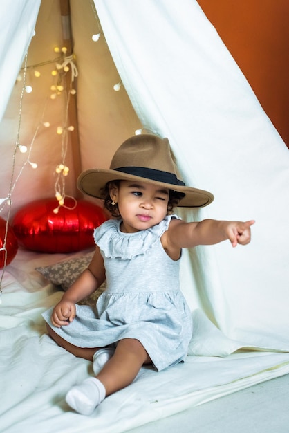 Garota negra afro-americana brinca em uma barraca de tenda com um chapéu mostrando uma infância feliz de dedo