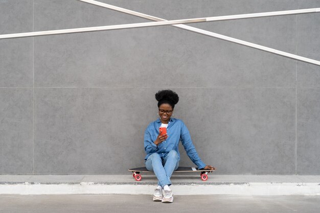 Garota negra feliz digite uma mensagem no smartphone ou navegue na mídia social via internet, sentada ao ar livre