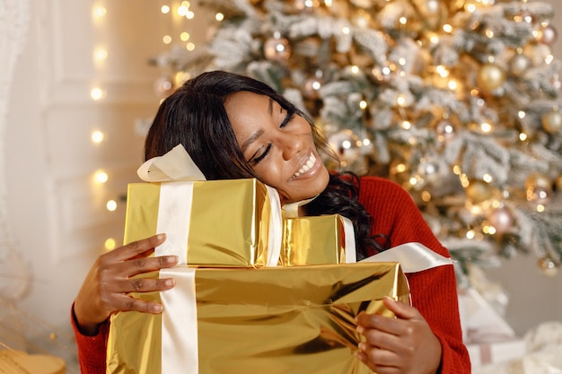 Garota negra perto de árvore de Natal abrindo o presente em casa
