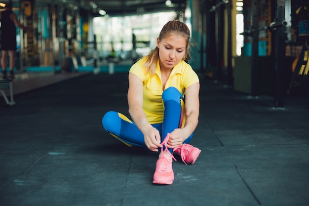 Garota no clube de fitness. Jovem atleta feminina sentada no chão e amarrou os cadarços