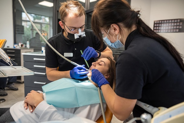 Garota no dentista com assistente recebe tratamento com a ajuda de equipamentos de última geração