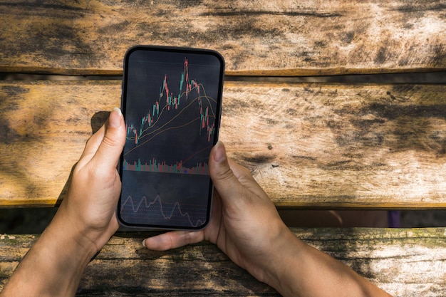 Garota no parque segurando um smartphone com gráfico do mercado financeiro de ações na tela Mesa de madeira rústica