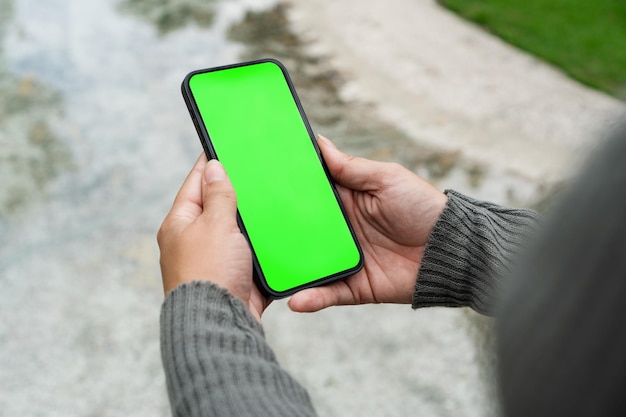 Garota no parque segurando um smartphone com tela verde Área verde de ponte de madeira e um lago artificial Chroma Key