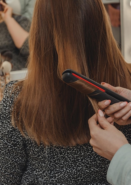 Garota no salão de beleza está fazendo seu cabelo estilo de cabelo feminino em ferro liso blog estética beleza cabeleireiros cabelo encaracolado ferro de ondulação espaço para texto