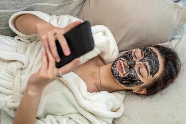 Foto garota no sofá com uma máscara cosmética feita de argila no rosto relaxa. o conceito de uma garota em uma máscara cosmética