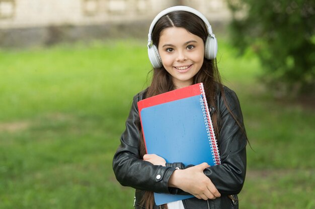 Garota ouvindo áudio carrega livros didáticos a caminho do conceito de clube escolar escolar