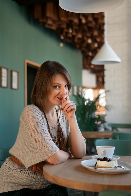 Garota paqueradora senta-se à mesa no café Jovem mulher no café com uma xícara de café com leite ou cappuccino e sobremesa