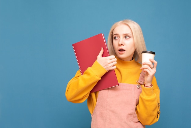 garota parada com um bloco de notas e uma xícara de café nas mãos, olha para o lado