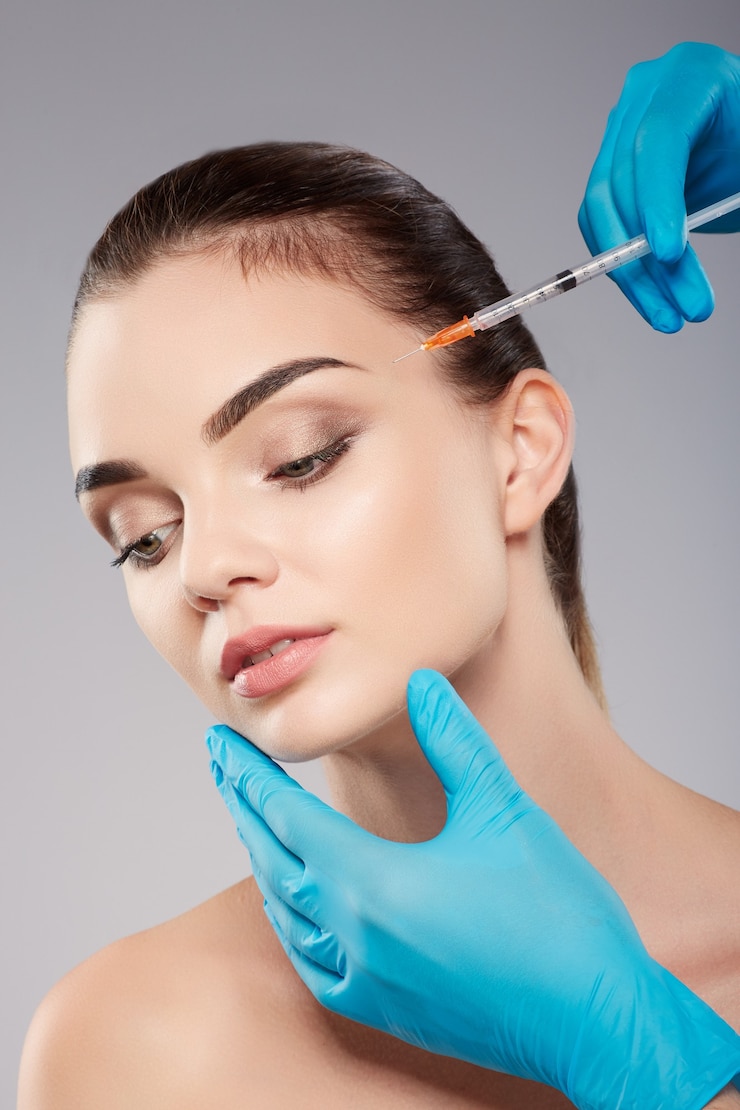 Foto garota perfeita com maquiagem nude no fundo do estúdio, as mãos do médico usando luvas azuis perto do rosto do paciente, segurando a seringa com botex perto do rosto, conceito de beleza, olhando para baixo.