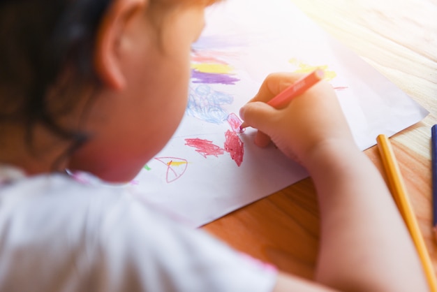 Garota pintando na folha de papel com lápis de cor sobre a mesa de madeira em casa