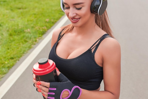 Garota posando com um shaker de nutrição esportiva no parque O conceito de um estilo de vida saudável Publicidade de estilo de fitness de equipamentos esportivos