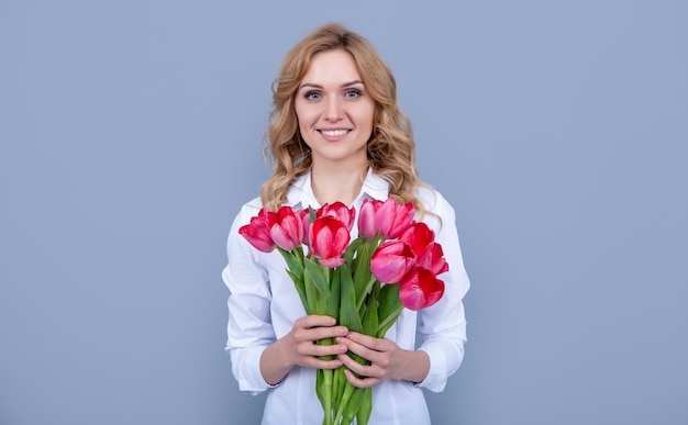 Garota positiva com flores de tulipa de primavera em fundo cinza