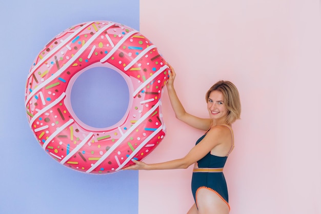 Garota positiva em traje de banho aproveitando o horário de verão com design de anel de rosquinha inflável