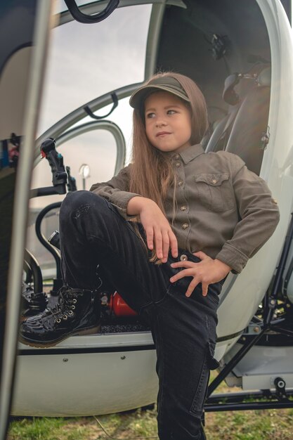 Garota pré-adolescente confiante em pé perto da cabine aberta do helicóptero