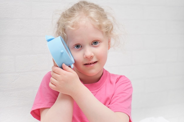 Garota pré-escolar em uma camiseta rosa ouve o tique-taque de um despertador conceito de sono saudável para crianças