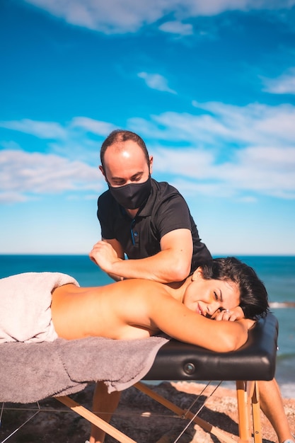Garota relaxada na massagem na costa perto da massagista do mar com máscara facial
