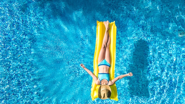 Garota relaxante na piscina, criança nada no colchão inflável e se diverte na água em férias em família, estância de férias tropical, vista aérea zangão de cima