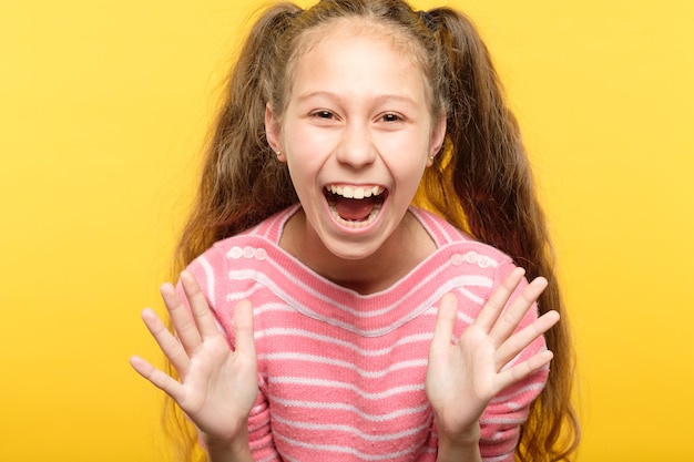 Garota rindo entusiasmada e superexcitada. retrato de criança em amarelo. emoção e expressão facial.