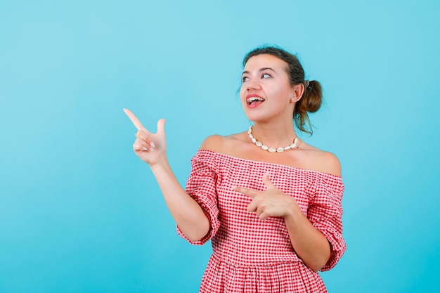 Garota rindo está olhando e apontando para cima com o dedo indicador sobre fundo azul