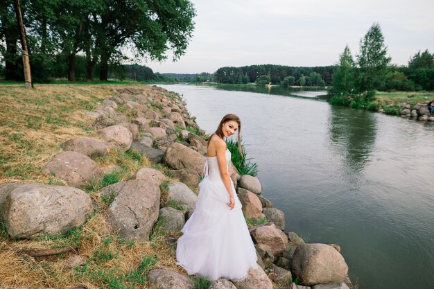 Garota romântica em um vestido branco macio na margem de um lago