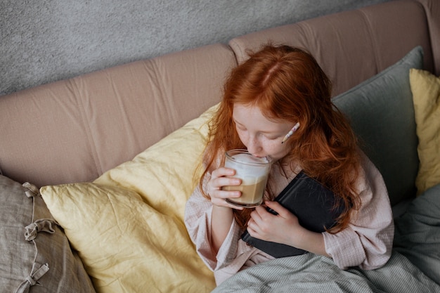 Garota ruiva bebe café na cama, colocando seu caderno de lado.